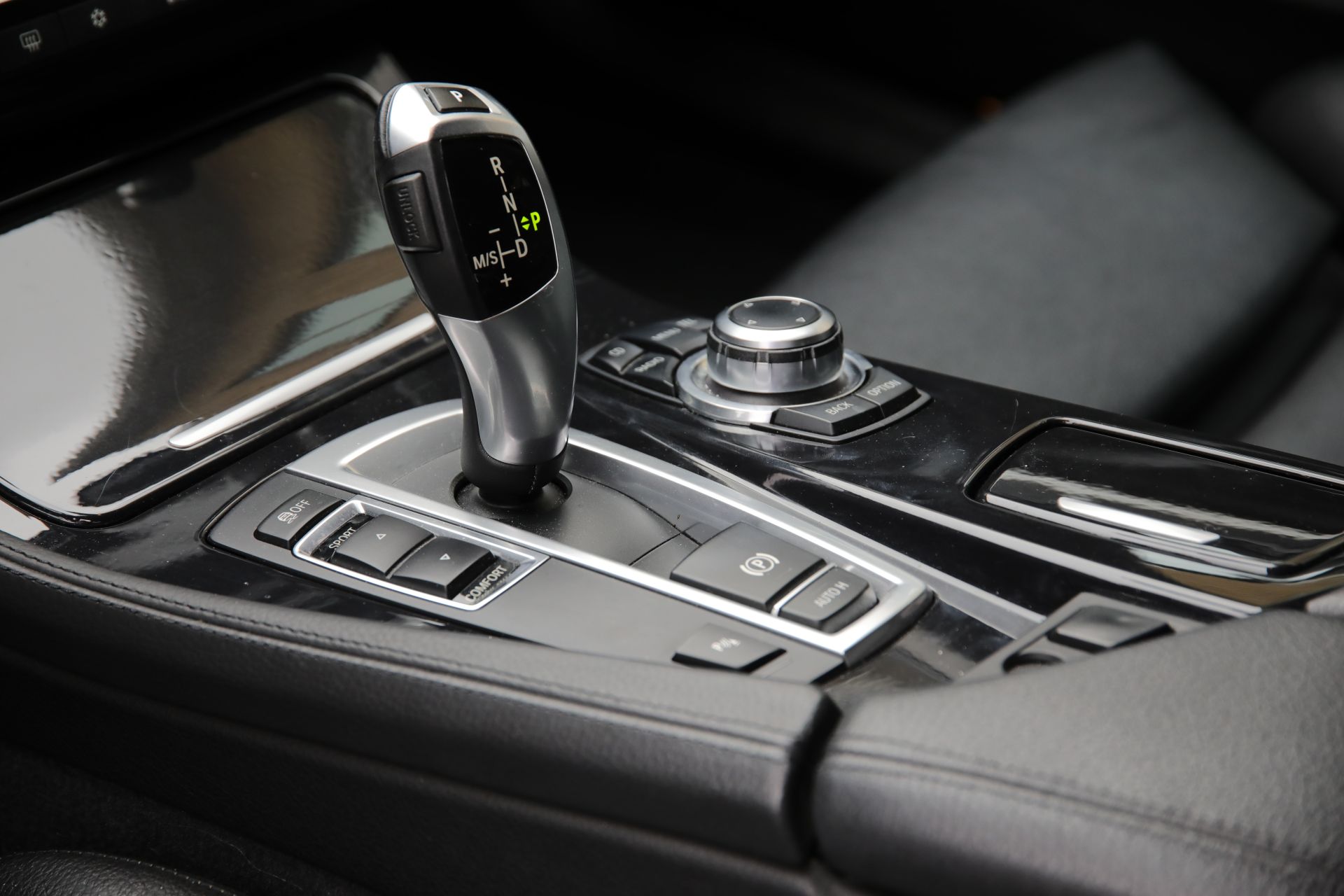 Moderne Mittelkonsole mit elektronischem Automatik-Schaltknauf, Fahrmodi-Tasten und iDrive-Controller in schwarzem Interieur.
